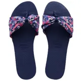 Sandalias tipo ojota Havaianas modelo You St Tropez, con base de goma azul marino y tira superior de tela con nudo decorativo y estampado floral en tonos rosas y blancos.