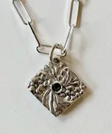 Collar de plata con cadena de eslabones tipo clip y dije romboidal texturizado con una piedra verde en el centro.