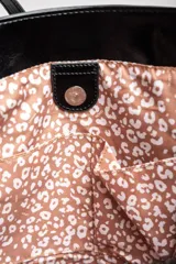 Bolso tipo tote de gran tamaño en color bordó con acabado brillante. Cuenta con doble asa de hombro y placa metálica decorativa con logo en la parte frontal.