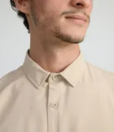 Camisa de manga larga color beige, con cuello camisero y dos bolsillos frontales con cierre en solapa.