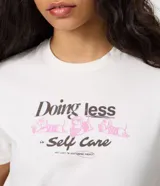 Remera de algodón con cuello redondo, mangas cortas y estampa en la espalda con diseño de un perro descansando en una reposera y la frase "Doing less is Self Care".