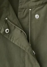 Chaqueta estilo militar verde militar, de diseño oversize, cuello alto, cierre frontal con cremallera y botones ocultos bajo tapeta, bolsillos con solapa y bolsillos de ribete en el pecho.