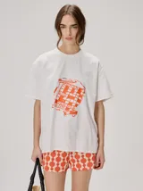 Remera oversize de corte cuadrado, color blanco con cuello redondo y estampa retro centrada en tono naranja.