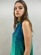Blusa de satén con escote halter y cuello elevado anudado lateralmente. Presenta un diseño estampado degradado en tonos verde esmeralda y azul, con corte holgado y caída fluida.