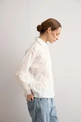 Camisa celeste con apliques florales bordados, cuello camisero, manga larga y cierre frontal de botones.