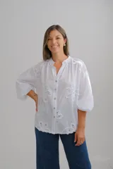 Blusa blanca de algodón con cuello mao, cierre frontal de botones y mangas tres cuartos abullonadas. Presenta un delicado diseño de bordado suizo con motivos florales en relieve a lo largo de toda la prenda.