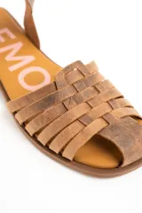 Sandalias cangrejeras de cuero color marrón, con diseño de tiras cruzadas en la parte delantera, suela plana y tira ajustable en el tobillo con hebilla metálica.