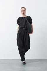 Pantalón baggy negro de silueta relajada con volumen amplio y caída fluida. Presenta detalles de ajuste con hebillas metálicas en el bajo y un cinturón de tela con hebilla metálica en la cintura.