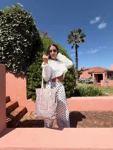 Bolso tipo tote bag de símil cuero color rosa pálido, con asas dobles y detalles de costura en color beige claro. Presenta un bolsillo frontal rectangular aplicado y herrajes metálicos.