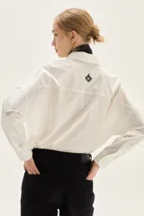 Camisa blanca de corte oversize, confeccionada en algodón, con cuello clásico y cierre frontal de botones. Presenta un bordado de corazones en el pecho.