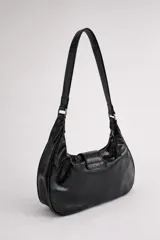 Cartera de hombro de tamaño compacto con acabado texturizado efecto cuero desgastado. Presenta un diseño con cierre superior, bolsillos frontales con cierre y una solapa central decorativa con hebilla metálica. Incluye asa fija para llevar al hombro.