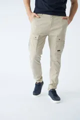Pantalón cargo de corte slim, color beige, con bolsillos laterales con solapa y botones, cierre frontal con botón y pasacintos.