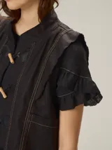 Chaleco negro con diseño de alamares frontales, costuras a la vista en contraste y volados en los hombros.