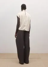 Blusa de seda color blanco marfil, con cuello alto drapeado y detalle de bufanda integrada al cuello. De manga larga con puños ajustados mediante tiras.