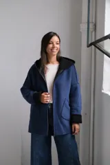 Tapado de paño azul con capucha, diseño de corte holgado y largo a la cadera. Presenta detalles en color negro en el interior, bordes y puños, con bolsillos frontales amplios y cierre frontal.