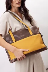 Cartera de hombro tipo portafolio confeccionada en cuero vacuno, con diseño estructurado que combina marrón liso y un panel frontal en cuero texturizado color mostaza. Posee doble asa larga y cierre superior.