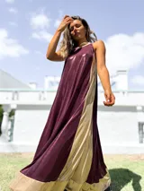 Vestido largo de fiesta con diseño bicolor, presentando un panel frontal en color bordó y paneles laterales en color dorado. Confeccionado en tela brillante con caída fluida, presenta escote halter y corte holgado.