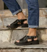 Sandalia de cuero vacuno color negro, con suela de goma deportiva, hebilla al tobillo y horma ancha.