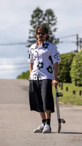 Camisa de manga corta, color blanco, con estampado de flores grandes en verde oscuro. Tiene cuello camisero y cierre frontal de botones.