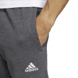 Pantalón de jogging gris con cintura elástica ajustable con cordón, bolsillos laterales y puños acanalados. Diseño con tres rayas blancas verticales a los costados y logo de Adidas bordado en blanco.