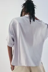 Camisa de manga corta color marrón oscuro, con cuello solapa, corte fluido y cierre frontal oculto con botones.
