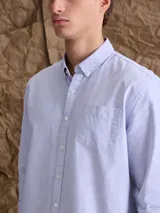 Camisa de corte clásico confeccionada en tejido Oxford de algodón, con cuello camisero, cierre frontal de botones y bolsillo en el pecho.