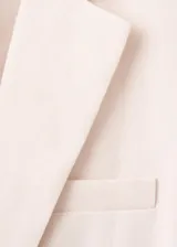 Blazer de lino color beige, de diseño recto con cuello en V, solapas con muesca, mangas largas, bolsillos de ribete delanteros y cierre frontal de un botón.