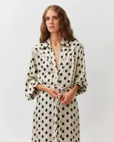 Vestido camisero largo de viscosa y seda, color blanco con estampado de lunares negros. Presenta cuello camisero, mangas largas abullonadas y un cinturón ajustable del mismo género.