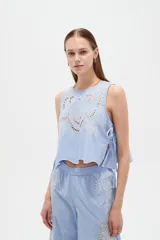 Musculosa de algodón color celeste, con cuello redondo y detalles bordados en tono blanco con diseño de broderie en la parte frontal. Cuenta con cordones laterales para ajustar.