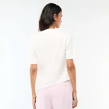 Camiseta blanca de manga corta y cuello redondo, con diseño drapeado en el lateral y detalle de adorno metálico dorado en la cintura.