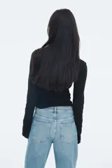 Top ajustado de punto acanalado suave, color negro, con cuello alto y mangas largas acampanadas.