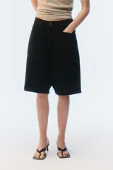 Bermuda oversize de denim color negro, con diseño de cinco bolsillos, cierre de botón y ojal, y ruedo deshilachado.