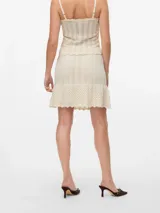 Pollera corta tejida en punto calado, color beige, con tiro medio, cintura elástica con cordón ajustable y ruedo con volado.