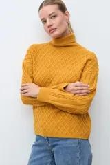 Polera de tejido de punto color ocre con cuello alto, diseño de rombos en relieve en el frente y mangas con detalle de trenzas laterales.