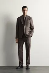 Pantalón de traje regular fit marrón con sutil estampado a cuadros, confeccionado en mezcla de lino y lana. Cuenta con bolsillos delanteros, bolsillos traseros de doble vivo con botón y raya marcada en el centro de las piernas.