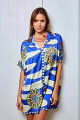 Camisola estampada con rayas horizontales azules y blancas, y flores amarillas, rojas y azules. Tiene cuello camisero, mangas cortas y cierre frontal con botones.