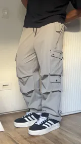 Pantalón cargo color gris claro, de corte amplio, con múltiples bolsillos con solapa y ajuste con cordón en la cintura.