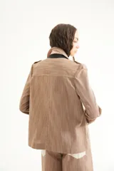 Chaqueta corta de inspiración motoquera color beige, confeccionada en lino fantasía, sin forro, con cierres decorativos, broches de presión y bolsillos delanteros funcionales. Presenta detalle bajo el cuello y en vueltas de mangas en color mostaza y rayas.