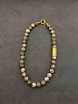 Collar de cuentas de piedras naturales en tonos tierra, con detalles de tubos dorados en los laterales.