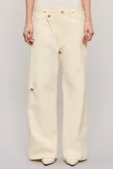 Pantalon de mezclilla color marfil con diseño cruzado asimétrico en la cintura, perneras anchas de corte relajado y detalles de roturas sutiles en la rodilla y el bolsillo.