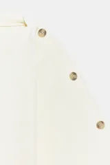 Jersey de punto blanco marfil, con cuello barco y mangas anchas tipo capa decoradas con botones a lo largo de los hombros y brazos.