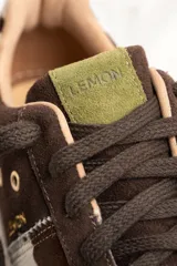 Zapatillas bajas de gamuza color marrón con cordones y suela de goma color crema. Presentan una franja lateral con estampado de vaca y el logo de la marca bordado en el lateral.