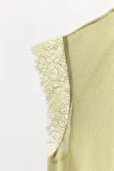 Body tipo blusa de georgette color verde oliva, con cuello redondo ajustable mediante lazada, mangas muy cortas con detalle de encaje y pliegues verticales en el delantero. Presenta una base de encaje en la parte inferior y cierre con botones a presión en el bajo.