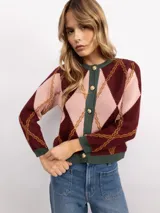 Cardigan de punto con patrón argyle en tonos bordó, rosa y verde. Presenta cuello redondo, cierre frontal con botones dorados y terminaciones en tejido acanalado verde.