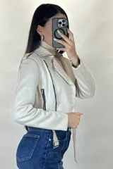 Chaqueta corta tipo biker confeccionada en gamuza color beige, con cierre frontal cruzado, solapas amplias, bolsillos con cierre y cinturón ajustable en la cintura.