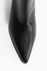 Botines cortos negros de cuero sintético, con punta fina y taco bajo y curvo. El diseño es liso y ajustado al tobillo.