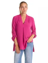 Blusa de tejido piqué color fucsia, con escote en V y pliegue central delantero. Presenta mangas largas con sistema de ajuste mediante presilla y botón, y tajos laterales en el ruedo.