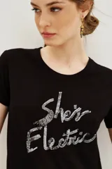 Remera de viscosa color negro, de corte clásico y manga corta, con estampa frontal de texto bordada en lentejuelas plateadas.