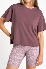 Remera deportiva color malva/ciruela, de manga corta y corte holgado, con cuello redondo y aberturas laterales en el ruedo.