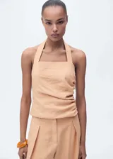 Top de cuello halter con diseño entallado, confeccionado en tejido de lyocell. Presenta un detalle fruncido en el lateral, cierre de botones en el cuello y cierre de cremallera lateral.